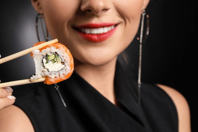 Mujer hermosa comiendo sushi con palillos