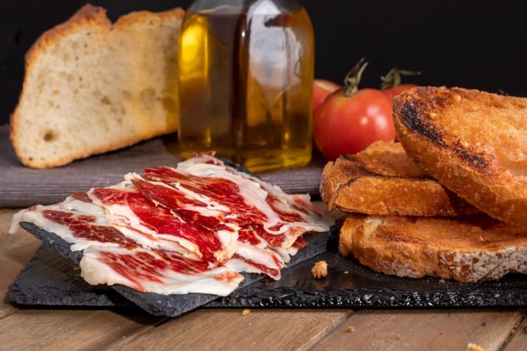 Jamón ibérico recién cortado, con pan y botella de aceite de oliva