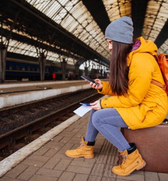 Bonita mujer joven esperando el tren en la estación, sentada en su maleta