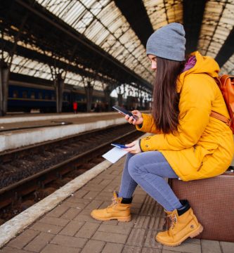 Bonita mujer joven esperando el tren en la estación, sentada en su maleta