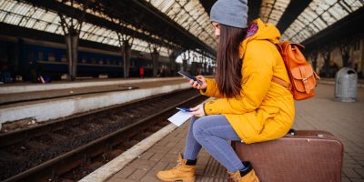Bonita mujer joven esperando el tren en la estación, sentada en su maleta