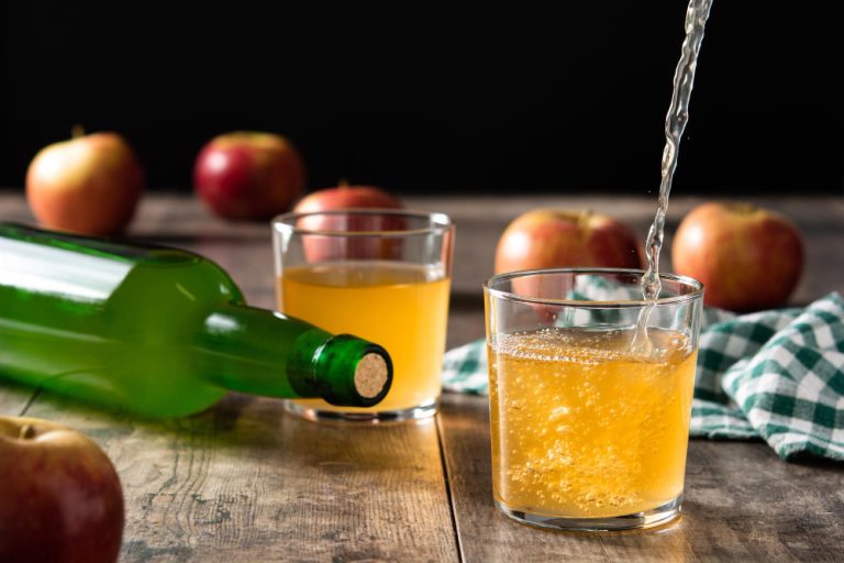 Botella de sidra tumbada y vasos de sidra llenos con manzanas al fondo
