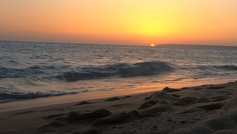 La puesta de sol sobre el océano en una playa arenosa.