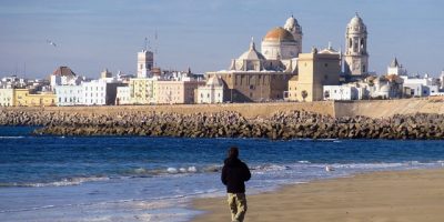 Un hombre camina por la playa de Cádiz con la ciudad al fondo.