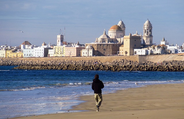 Un hombre camina por la playa de Cádiz con la ciudad al fondo.
