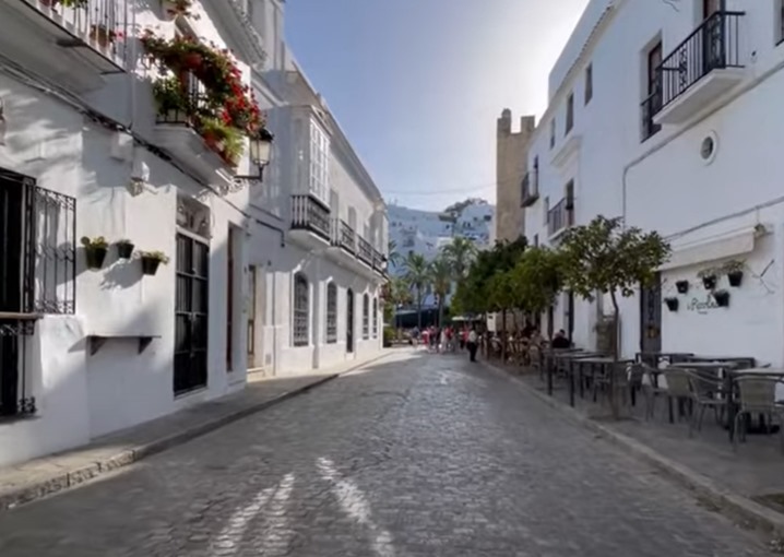 Una encantadora calle adoquinada en Vejer de la Frontera bordeada de edificios y mesas blancas.
