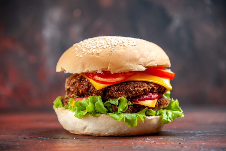 Una hamburguesa con queso, tomate y lechuga sobre un fondo oscuro, mostrando platos típicos de todo el mundo.