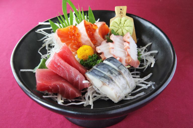 Una variedad de platos típicos de todo el mundo presentados en un bol negro, incluido el sashimi.